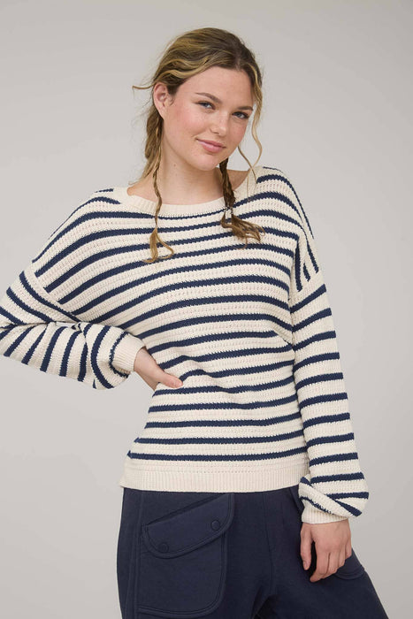 Woman wearing a striped sweater and dark pants against a plain background