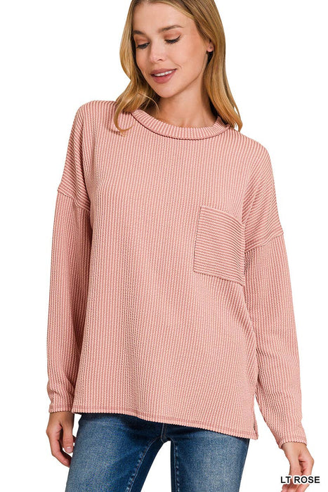 Woman wearing a light pink ribbed sweater with a pocket on a white background