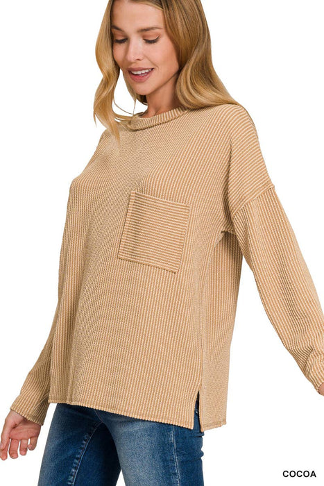 Woman wearing a beige ribbed sweater with a pocket on a white background